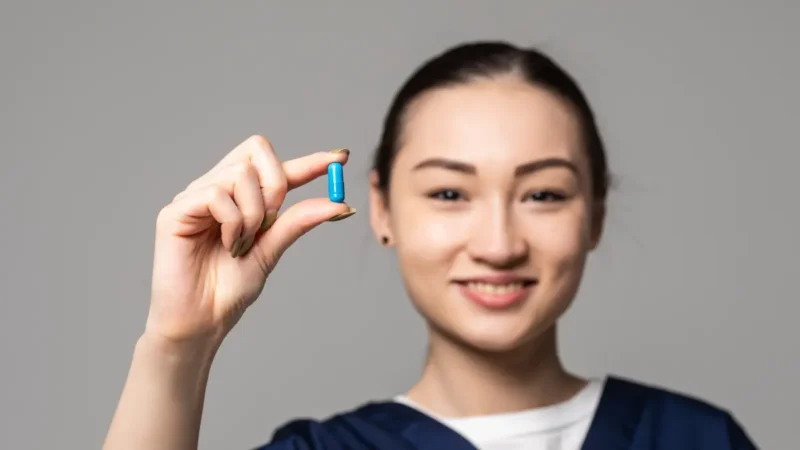 Person in medical scrubs holding a small blue capsule between fingers.