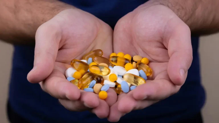 Hands holding multiple mixed pills and capsules, illustrating risk of dangerous drug interactions