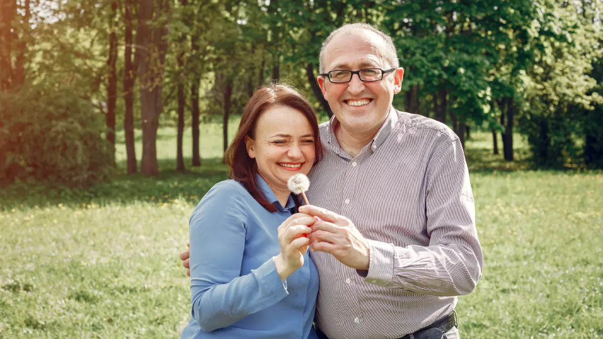 Smiling middle-aged couple standing close in a sunny forest clearing.