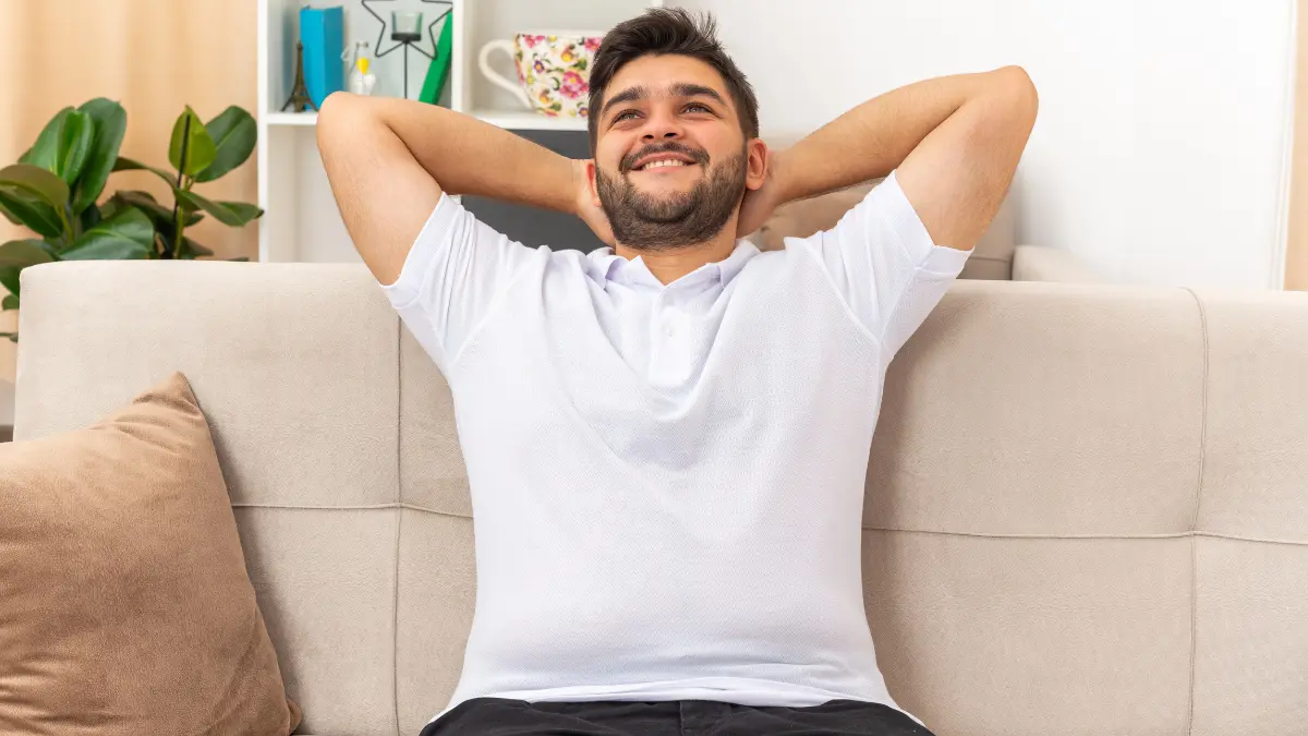 Man leaning back on a sofa with hands behind his head, looking relaxed.