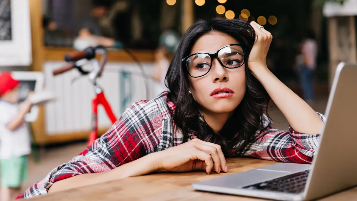 Young professional showing signs of workplace exhaustion and screen time fatigue with hand on head while using laptop