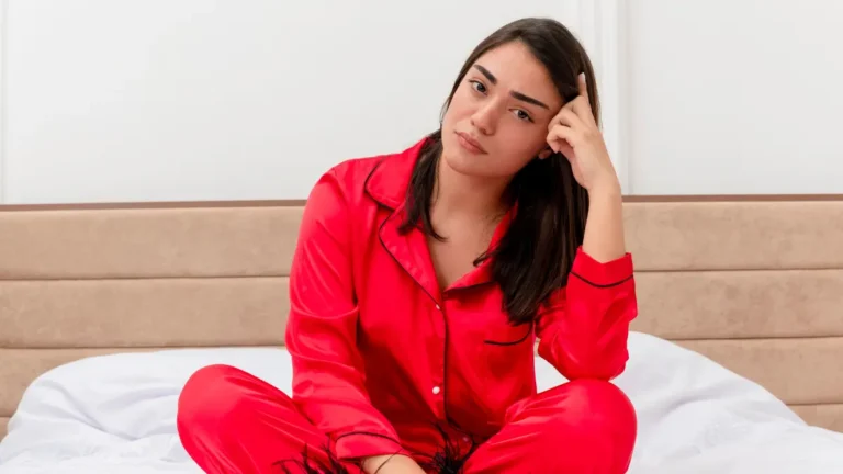 Woman experiencing year end emotional heaviness and December burnout sitting on bed in pajamas looking exhausted from holiday stress