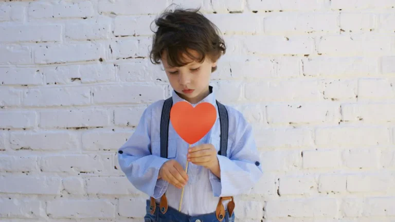 A child holds a red paper heart on a stick and looks down.