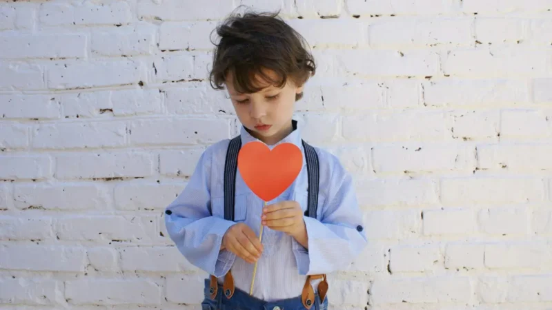 A child holds a red paper heart on a stick and looks down.