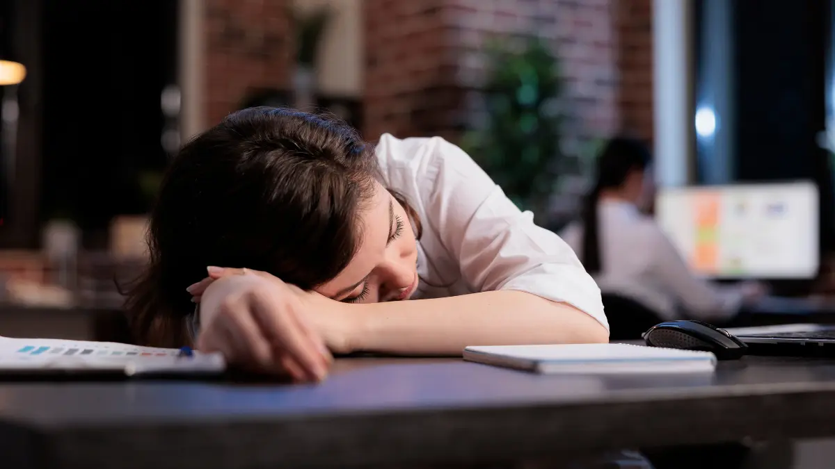 Tired office worker asleep on her arms at a desk after a long day