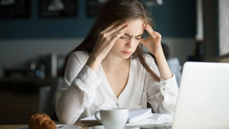 Woman holding her temples while feeling a wave of quiet fatigue at a café table