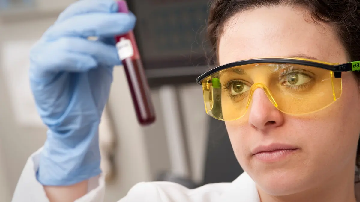 Scientist holding up a vial to analyze a Shield Blood Test sample in a laboratory.