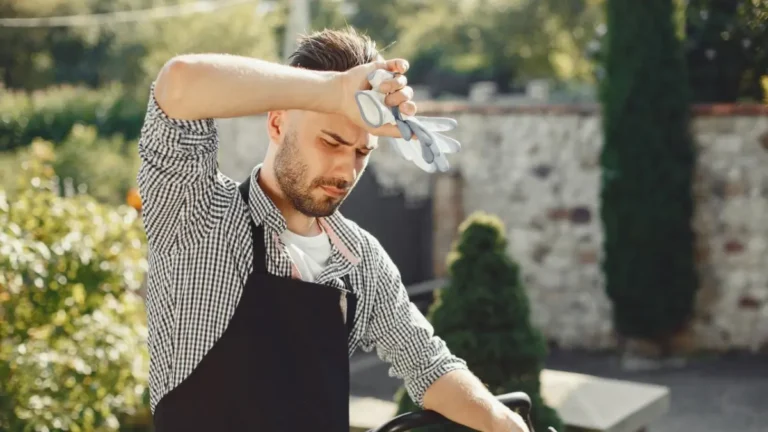 Man in an apron wiping sweat from his forehead while working outdoors in the summer heat