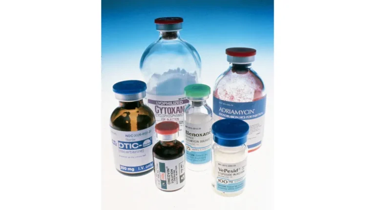 A variety of oncology prescription medicine vials resting over a blue gradient background, illustrating multi-drug plans affecting pancreatic cancer treatment cost.